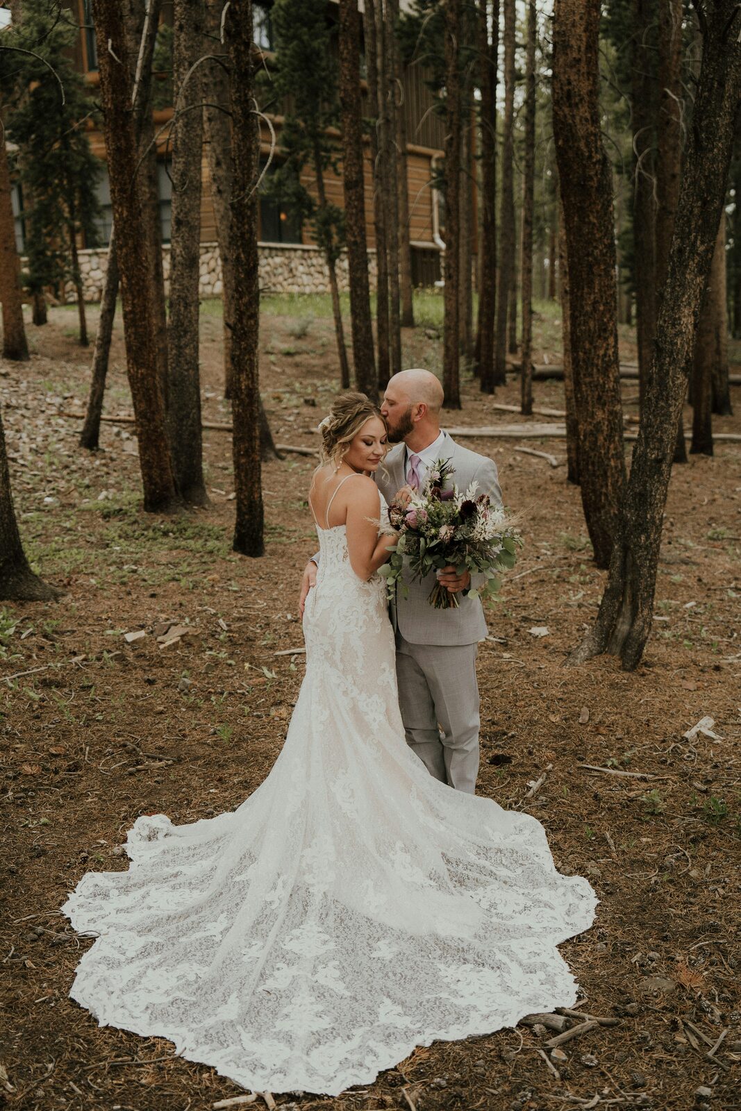Colorado bride and groom sharing a forehead kiss in a pine forest with a boho bouquet