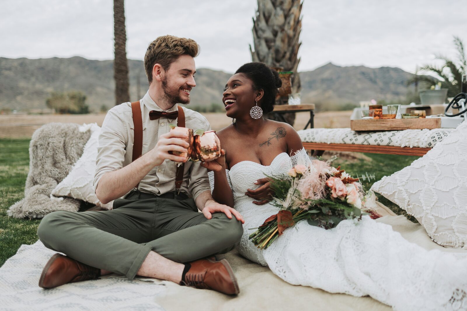 Arizona couple toasting with copper mugs at a boho desert wedding picnic after starting their prenup