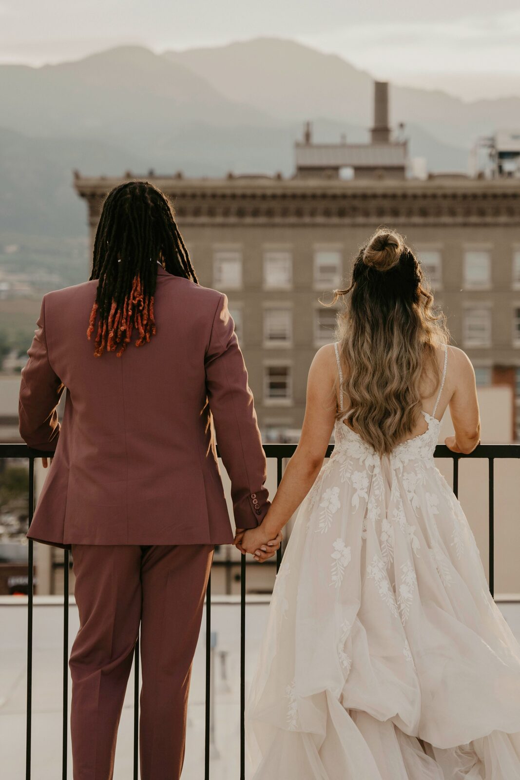 Interracial Colorado newlyweds on a rooftop with mountain views, seen from behind