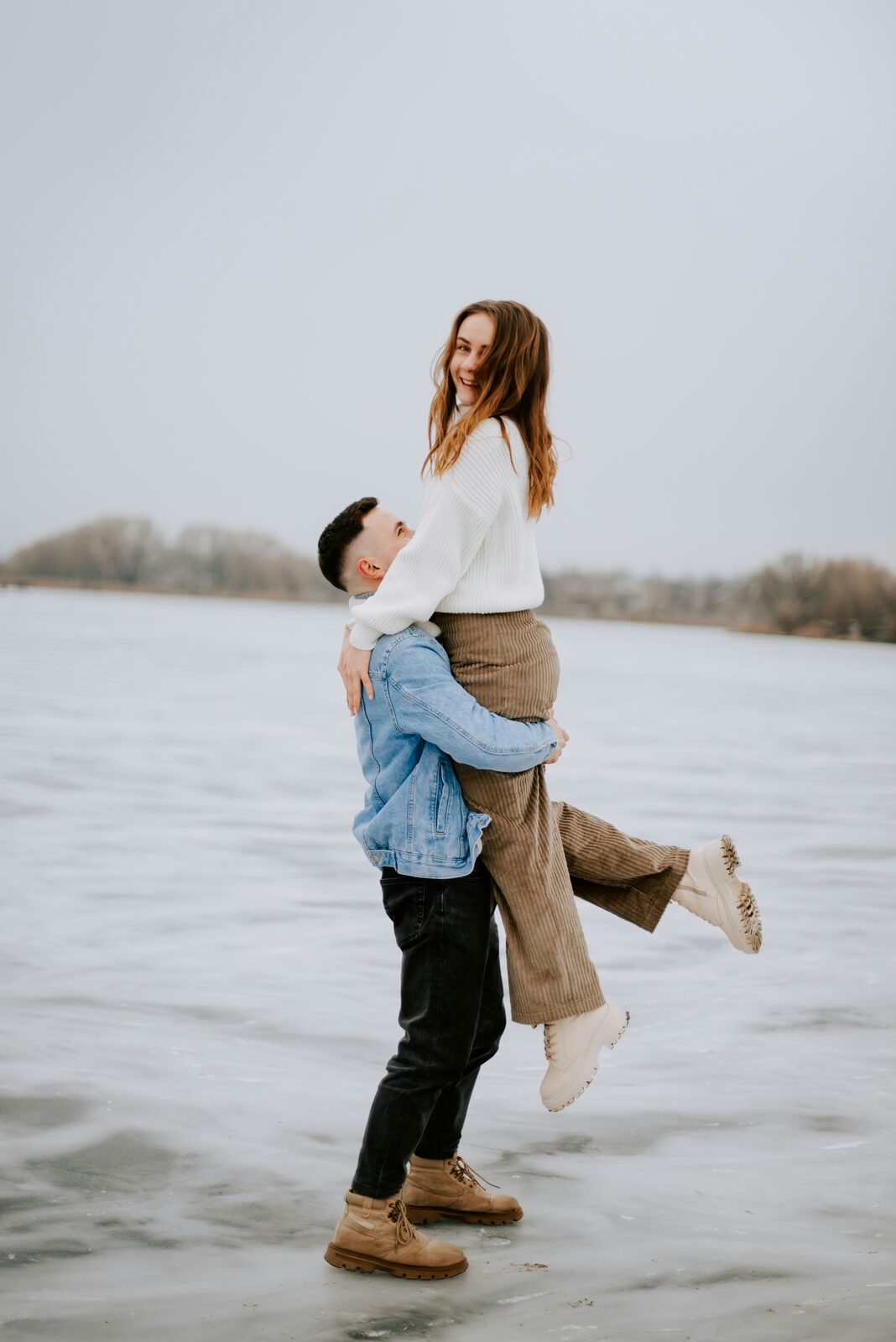 Virginia couple at a frozen lake in winter, one lifting the other during their engagement
