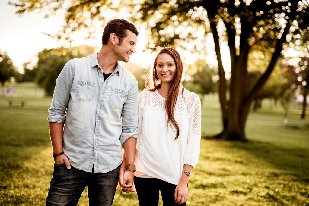 A couple walking hand in hand on a sunny day, with the man looking lovingly at his partner while she smiles at the camera.