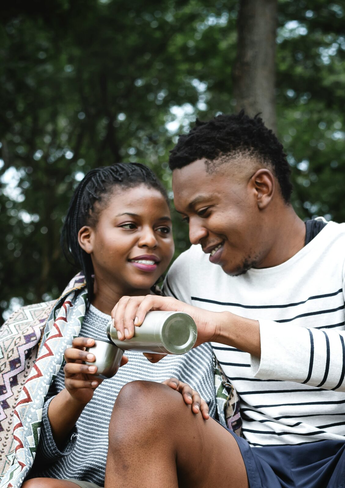 Minnesota couple pouring coffee from a thermos while camping, wrapped in a blanket