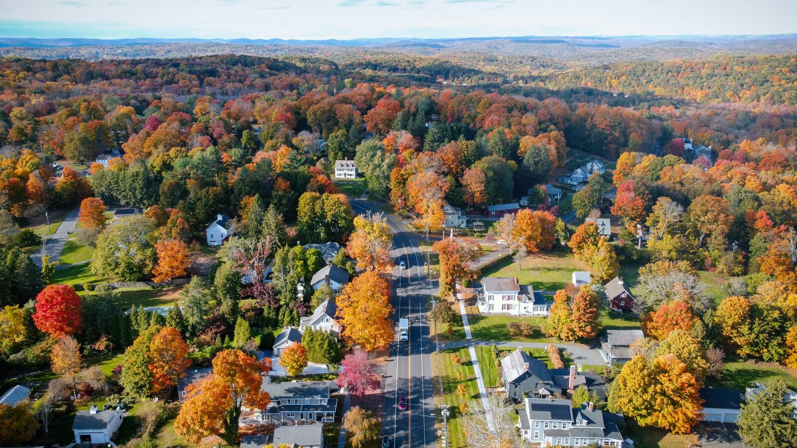 Aerial view of Connecticut fall foliage over a New England small town and country road in autumn