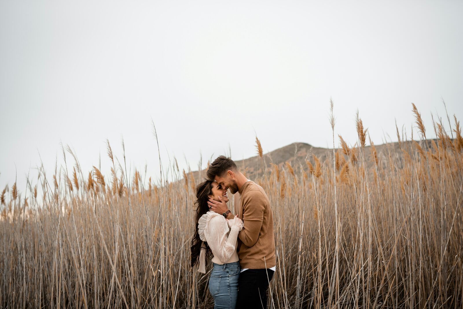Connecticut couple touching foreheads among pampas grass reeds, in a tan sweater and lace blouse