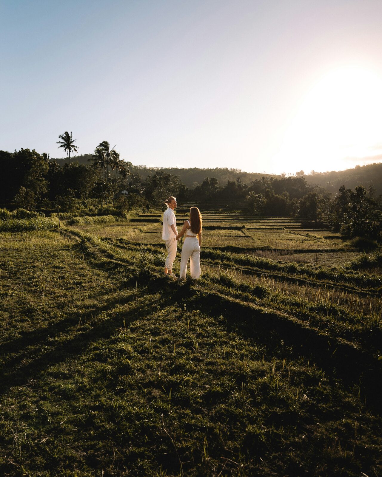 Connecticut couple holding hands at sunset on a rice terrace during a tropical honeymoon in white outfits