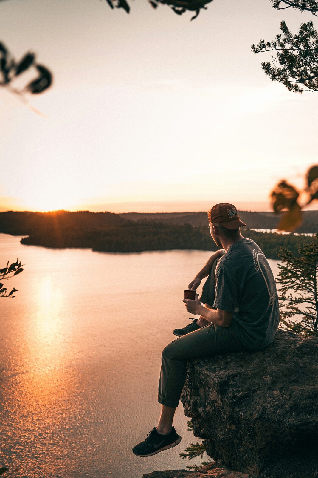 Man with a coffee on a rocky cliff above a Boundary Waters lake at sunset in northern Minnesota
