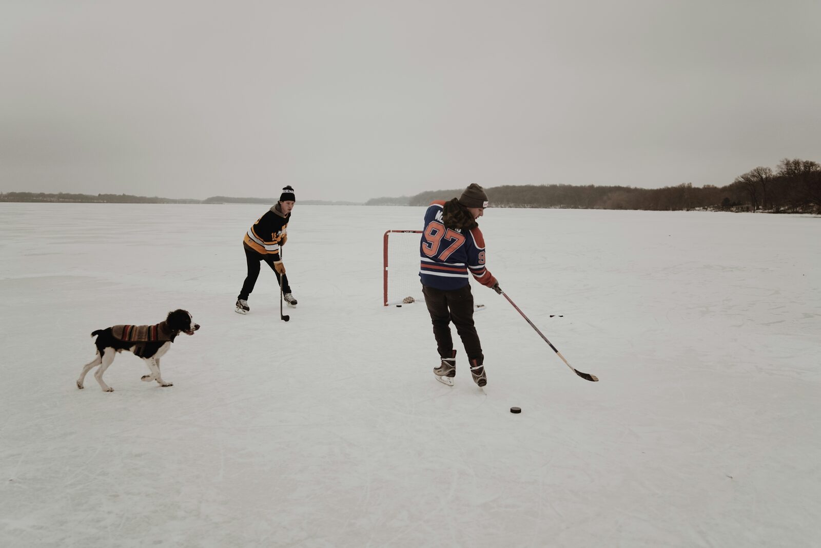 Minnesota couple in hockey jerseys with their dog on a frozen lake for a game of pond hockey