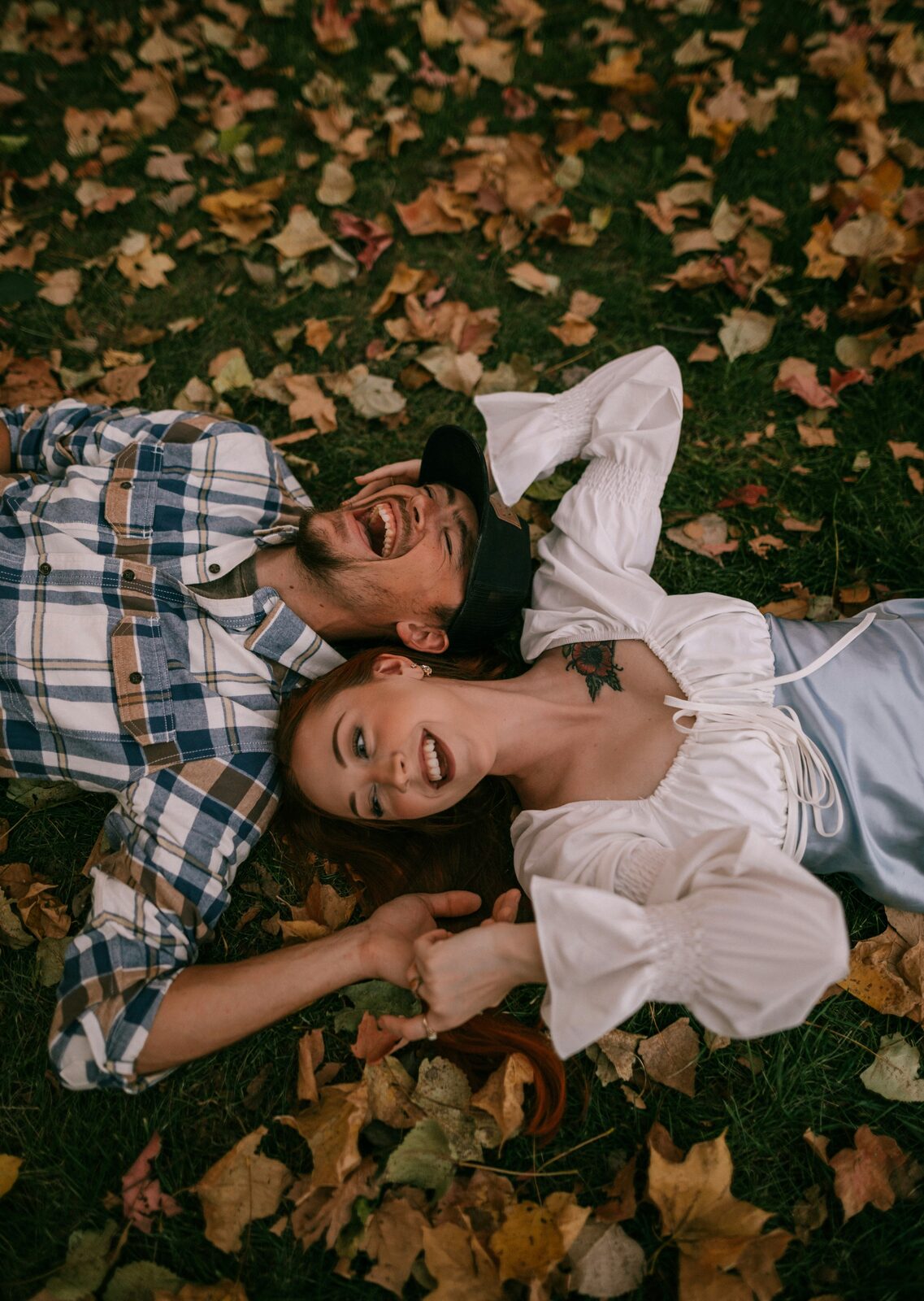 Connecticut couple laughing in fall leaves during their engagement, in a plaid shirt and white blouse