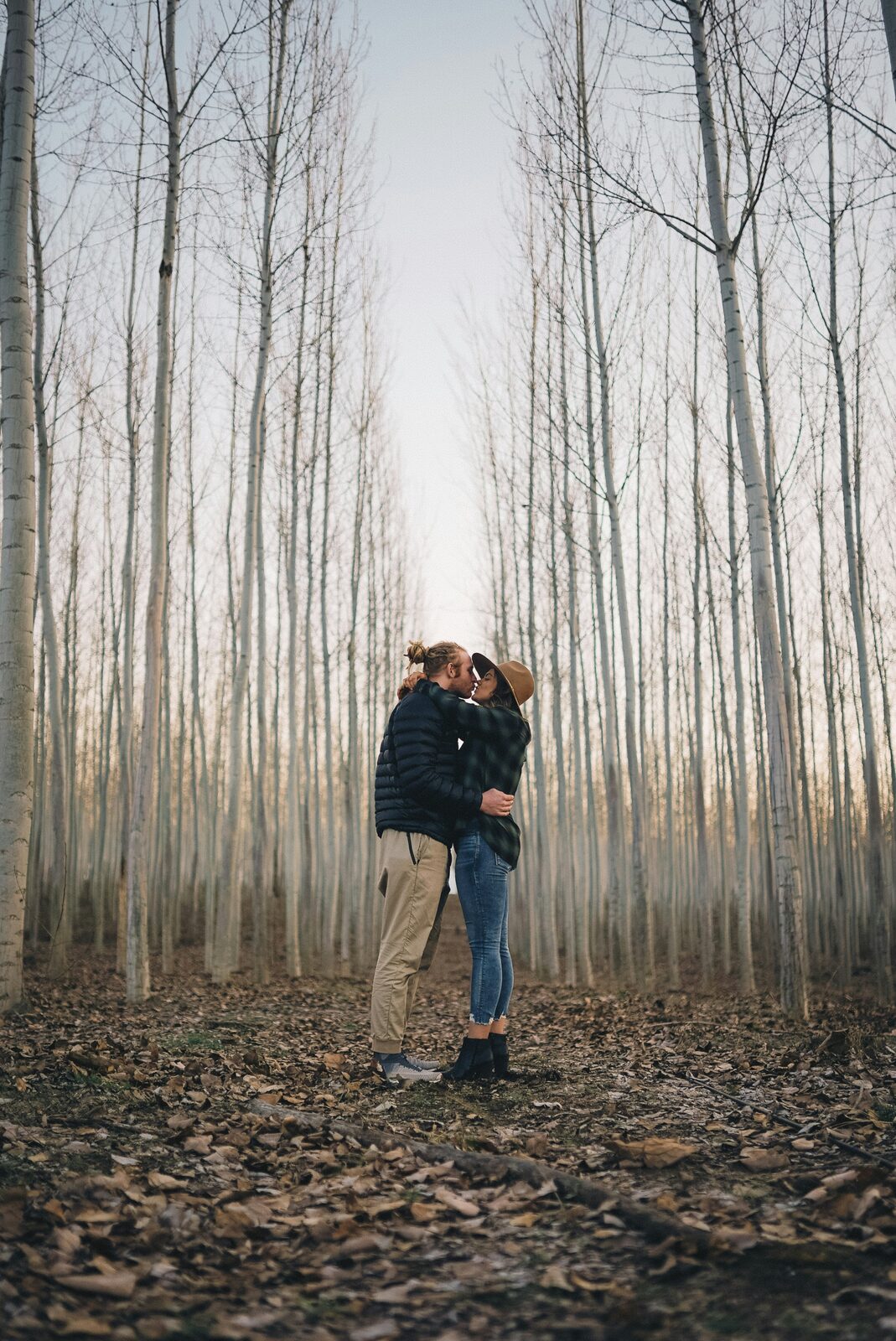Newly engaged Oregon couple kissing between rows of poplar trees on a Boardman tree farm, before building their prenup