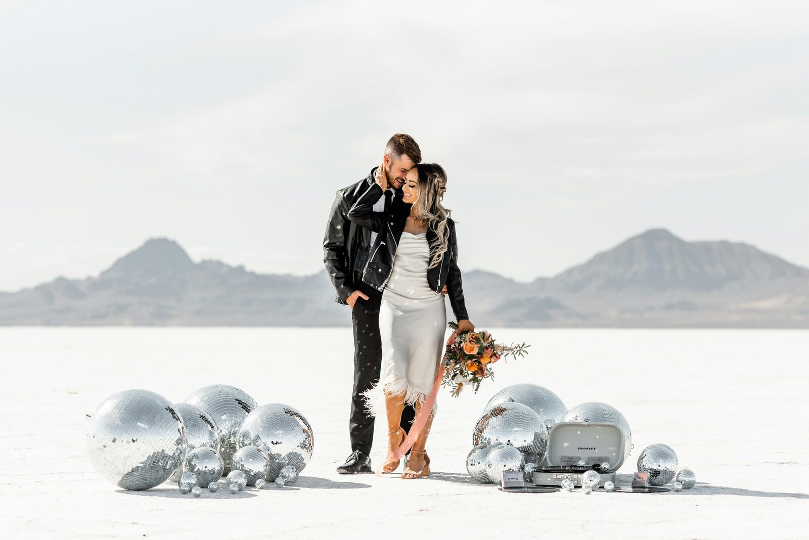 Utah couple in leather jackets embracing on the Bonneville Salt Flats beside disco balls, protected with a HelloPrenup prenuptial agreement