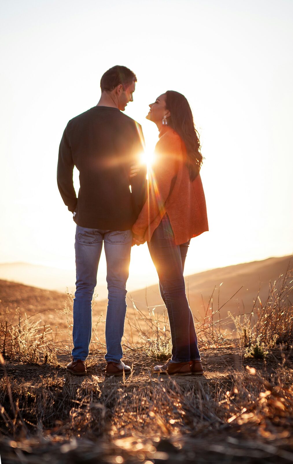 Engaged Oklahoma couple holding hands on a grassy hilltop at sunset, protected with a HelloPrenup prenuptial agreement