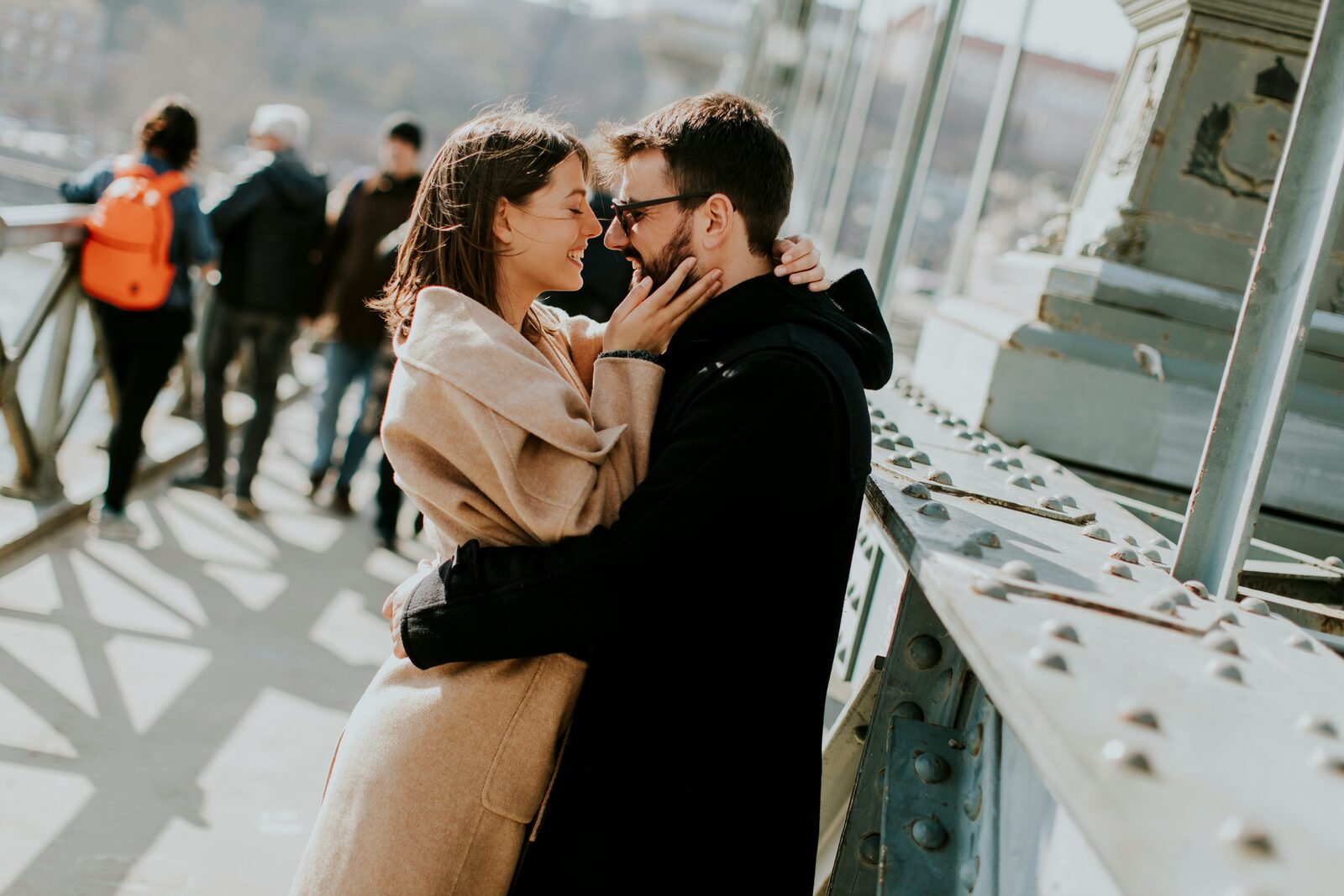 Engaged couple embracing on a bridge in winter coats, talking through how to get their prenup done