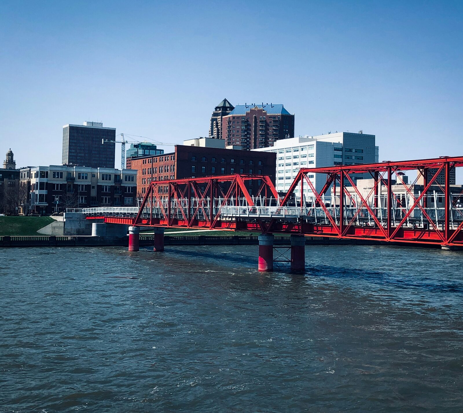 Downtown Des Moines, Iowa skyline with a red truss bridge over the river on a sunny day